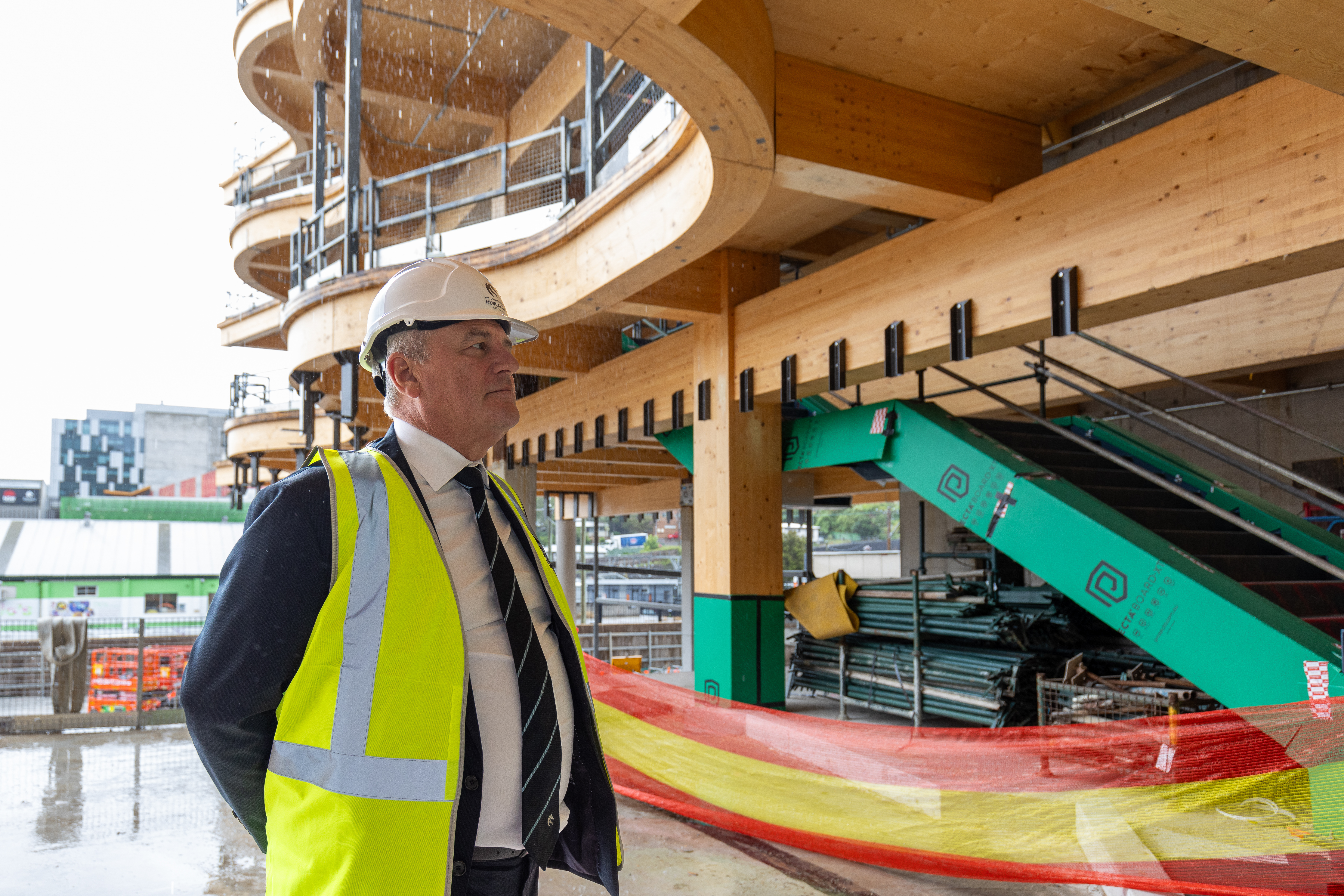 Vice Chancellor Alex Zelinsky is wearing a high-vis vest and hard hat as he looks out into the construction site of the new building