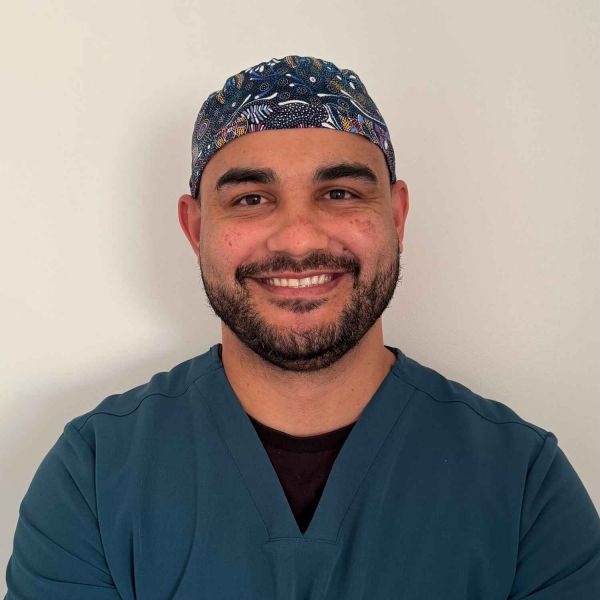 Kieran Cubby Indigenous male with dark brown hair and beard standing in navy scrubs smiling.