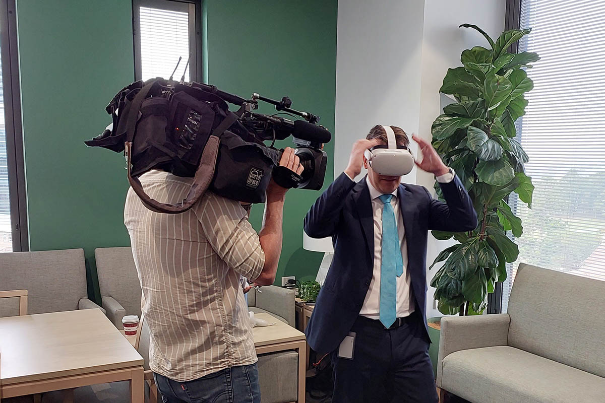 A man wearing VR goggles, and a cameraman videoing him