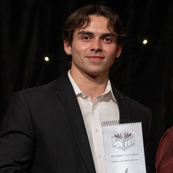 A person in a suit proudly holds an award certificate.. Journalism student Blair Wise wins 2025 Kennedy Awards Student of the Year