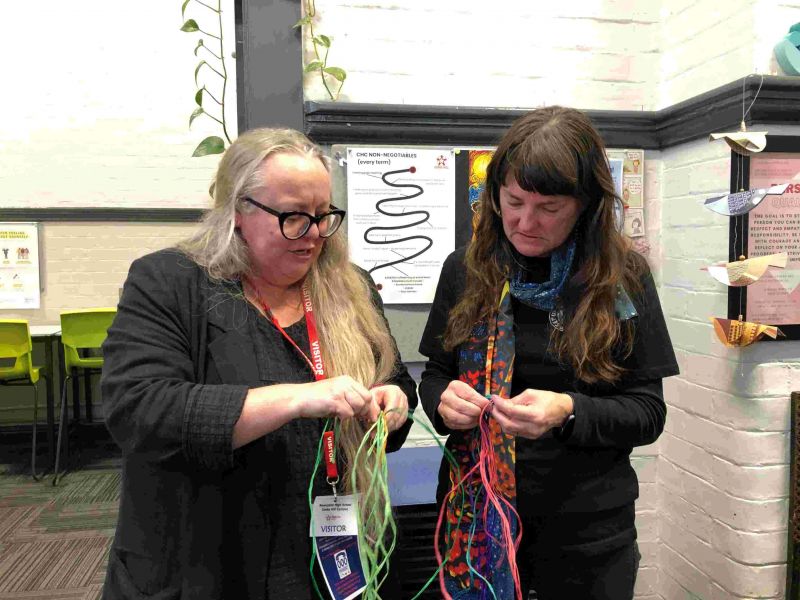 Two women standing together weaving tiny baskets