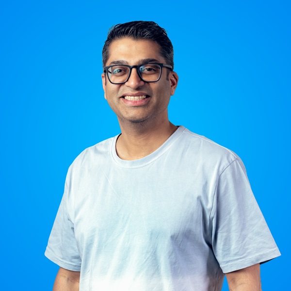 Man wearing glasses and smiling for the camera in front of a blue background