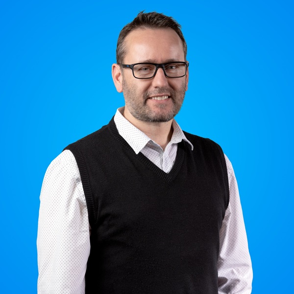 Man wearing glasses and smiling for the camera in front of a blue background