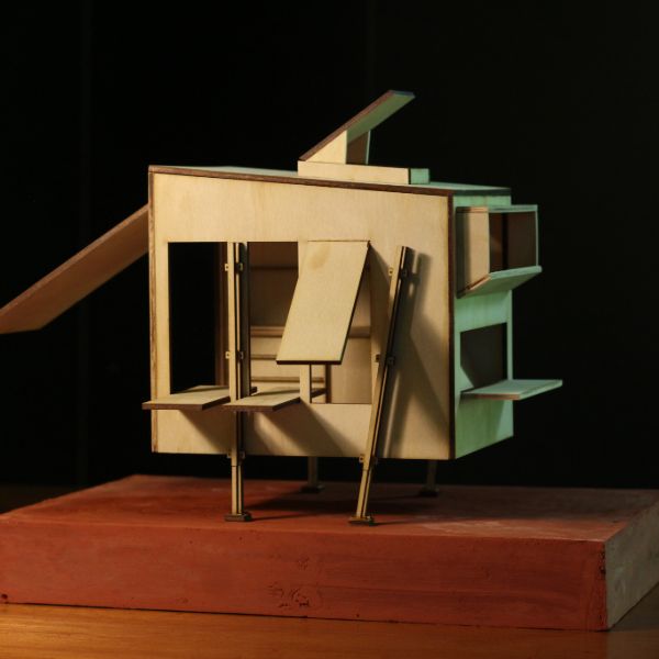 Wooden architectural model with geometric design, featuring multiple small platforms and overhangs on a rectangular base, lit dramatically from above.