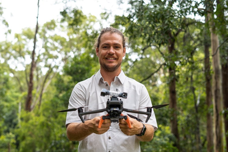 Dr Ryan Witt pictured holding a drone, smiling to camera