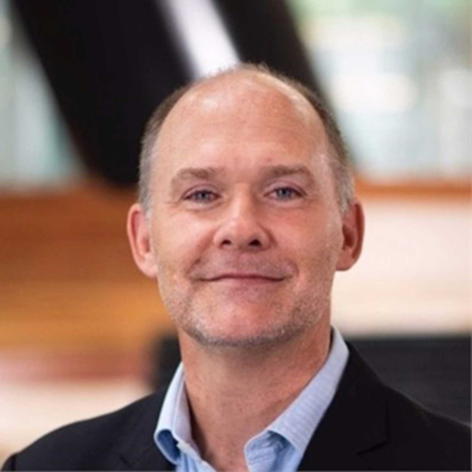 Man smiling at the camera, pictured from the chest and wearing a suit jacket