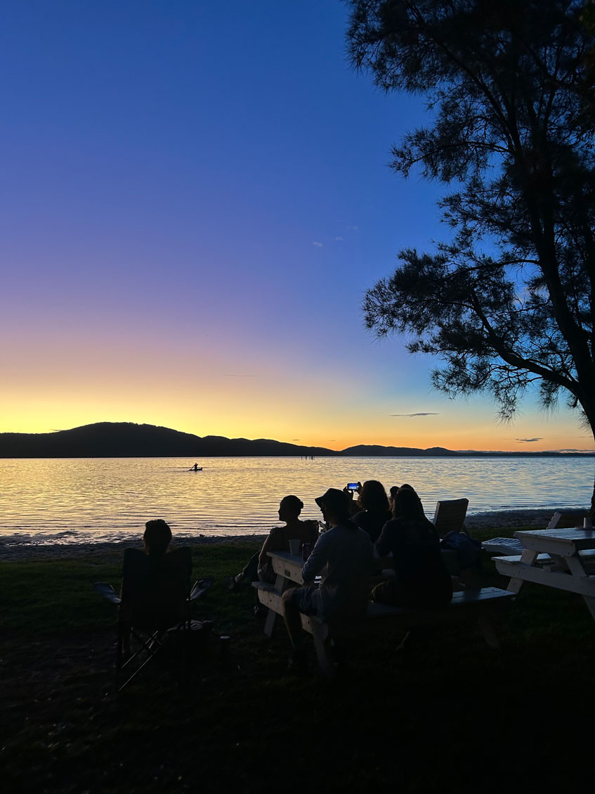 Silhouettes in front of a sunset over a body of water.