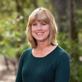 Victoria Haskins, blonde hair smiling in front of trees wearing dark green shirt. Anzac Commemoration Fellowship project highlighted