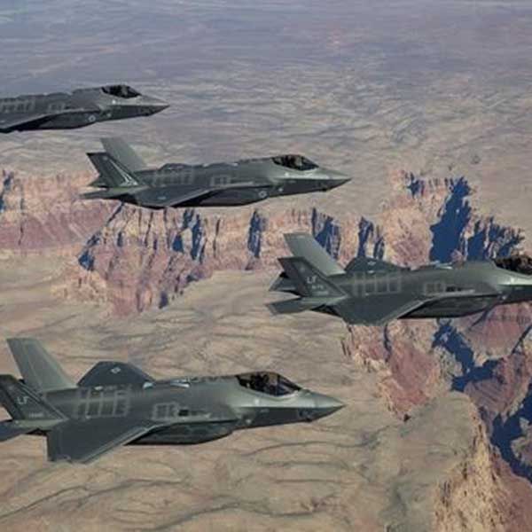 Four fighter jets flying above a canyon