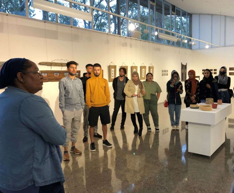 A woman in an art gallery talking to a group of young adults from different ethnic backgrounds