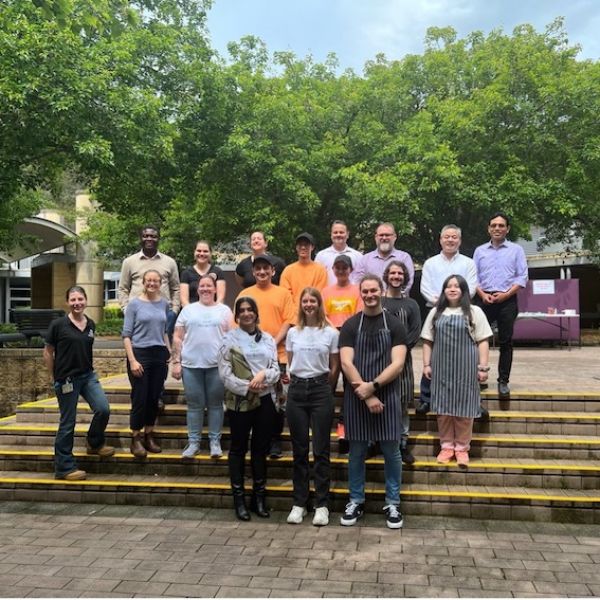 Group of staff and students standing on some steps, smiling to camera