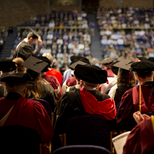 A picture of people at a graduation ceremony, someone walking across stage to receive the degree is visible