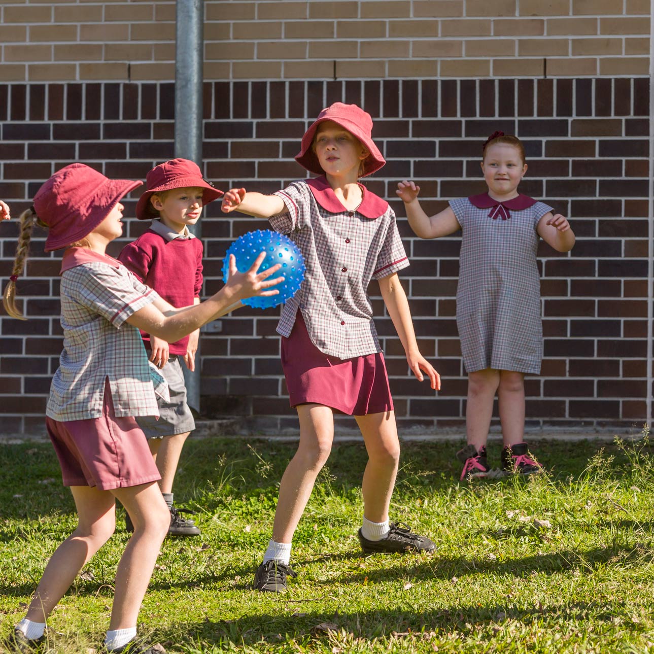 A group of kids in red school uniforms play with a blue ball on a grassy area^empty:{ds__assetid^as_asset:asset_name}