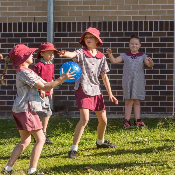 A group of kids in red school uniforms play with a blue ball on a grassy area