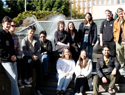 Approximately 10 people standing around a fountain, smiling