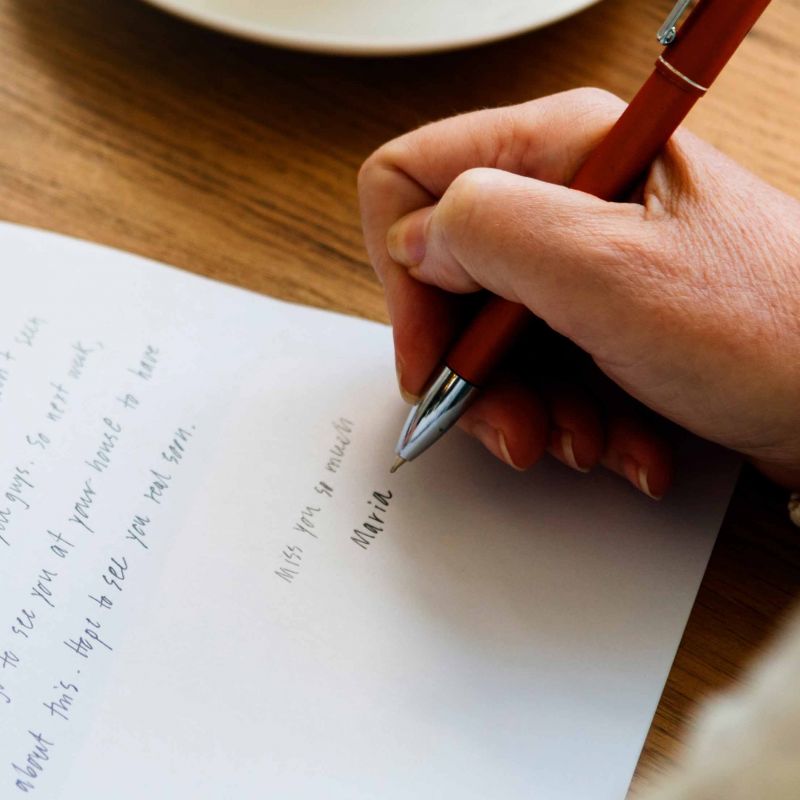 Hand holding a pen writing a letter on a wooden table