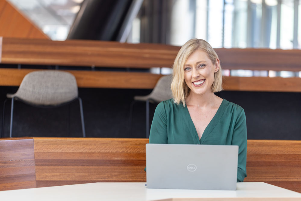 A woman smiling sitting at a table with a laptop