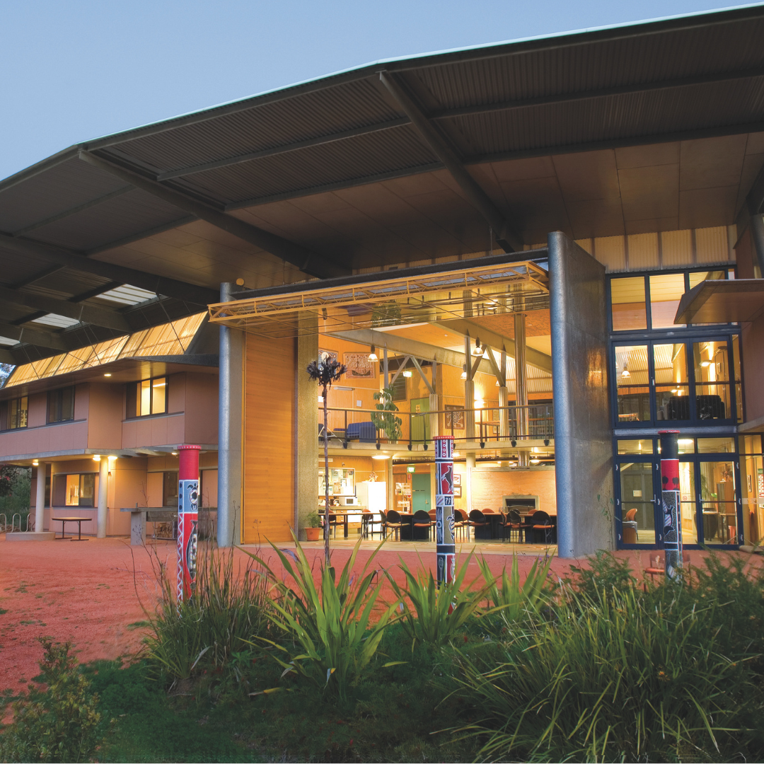 Wollotuka building at Callaghan, featuring Aboriginal totem poles and native landscaping at dusk.