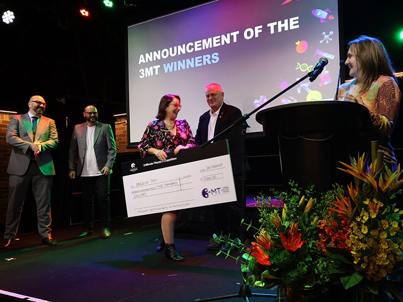 Woman receiving novelty check on stage, surrounded by judges