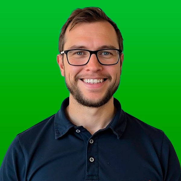 Man wearing glasses and smiling for the camera in front of a green background