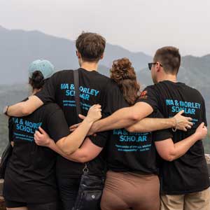 Four students are seen from behind, arms linked together looking over the Great Wall of China, with Ma & Morley shirt logos visible