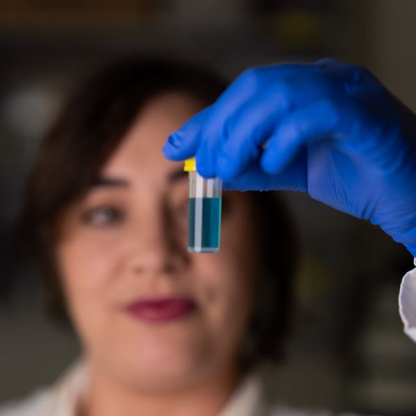 researcher is pictured holding up a sample of blue liquid in the front of the frame