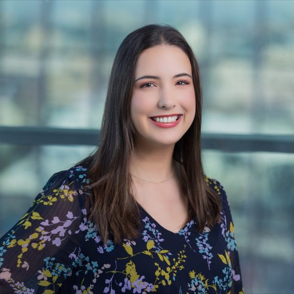 Female with long brown hair wearing a navy and floral top smiling.