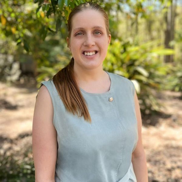Claudia standing outside, in front of trees, smiling at the camera
