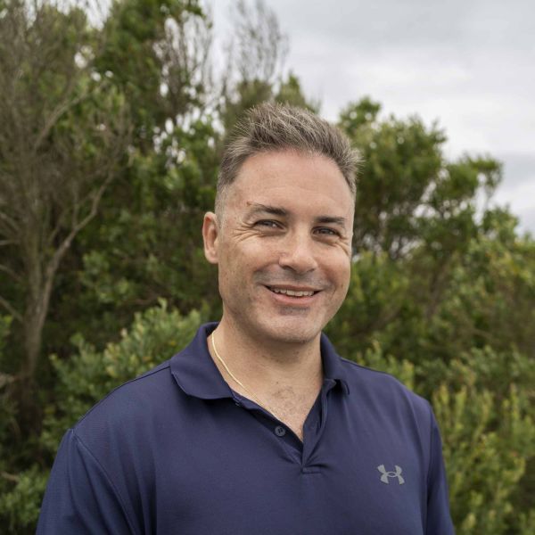 Tim standing on front of lots of greenery and smiling.