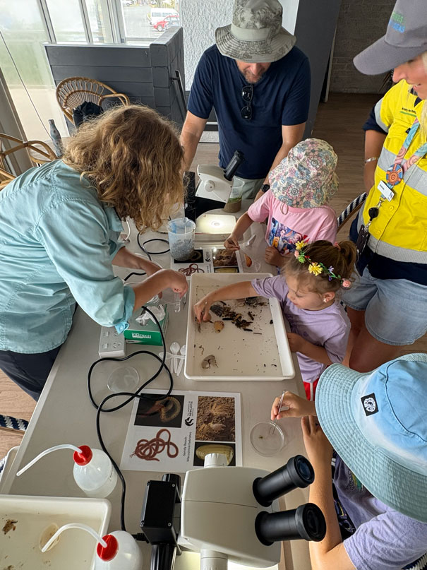 Community members look at creatures and beach materials in a white container