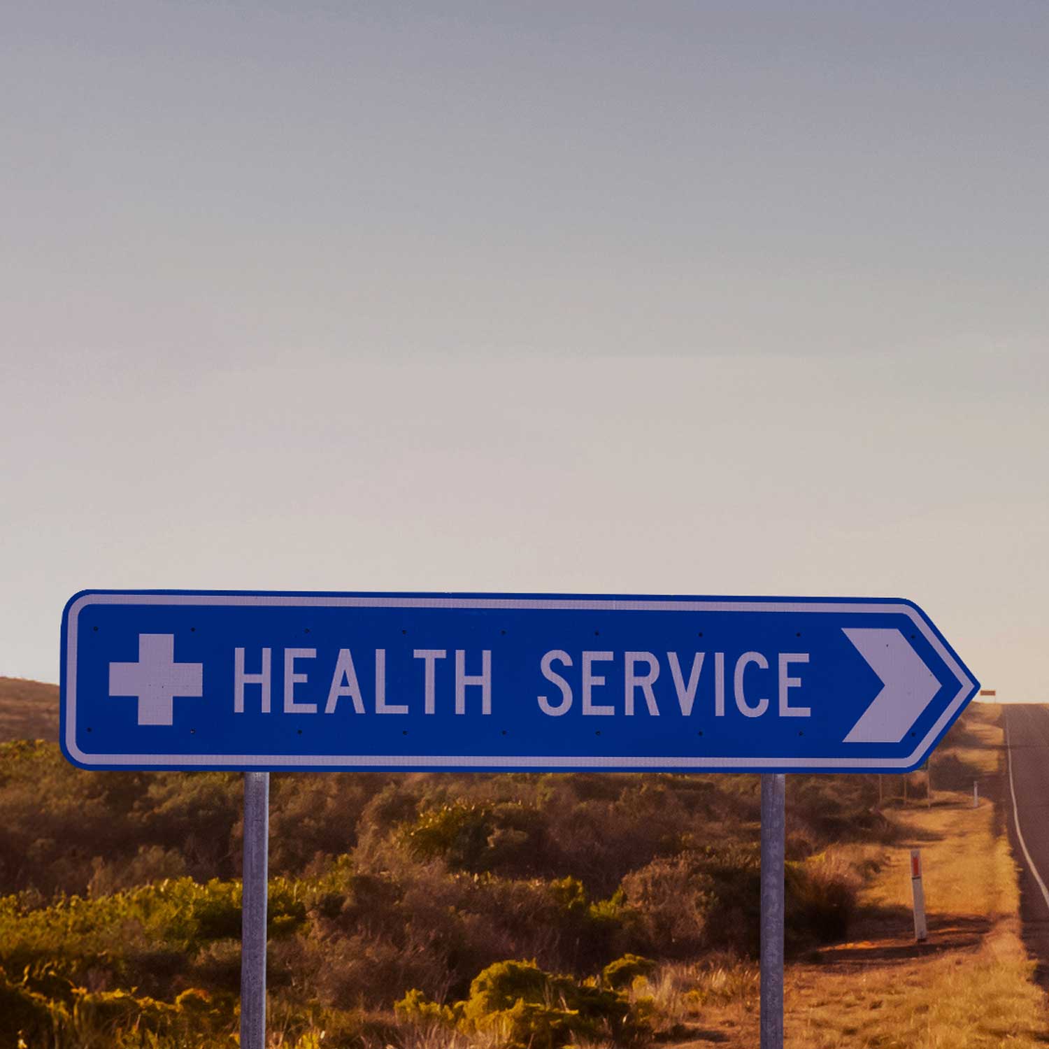 A road sign with text 'Health Service' along a highway road with desert terrain.