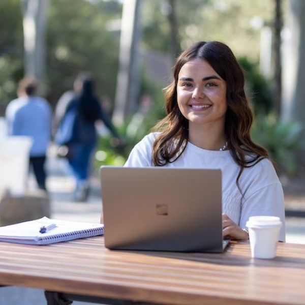 Student sitting at an outdoor bench on their laptop
