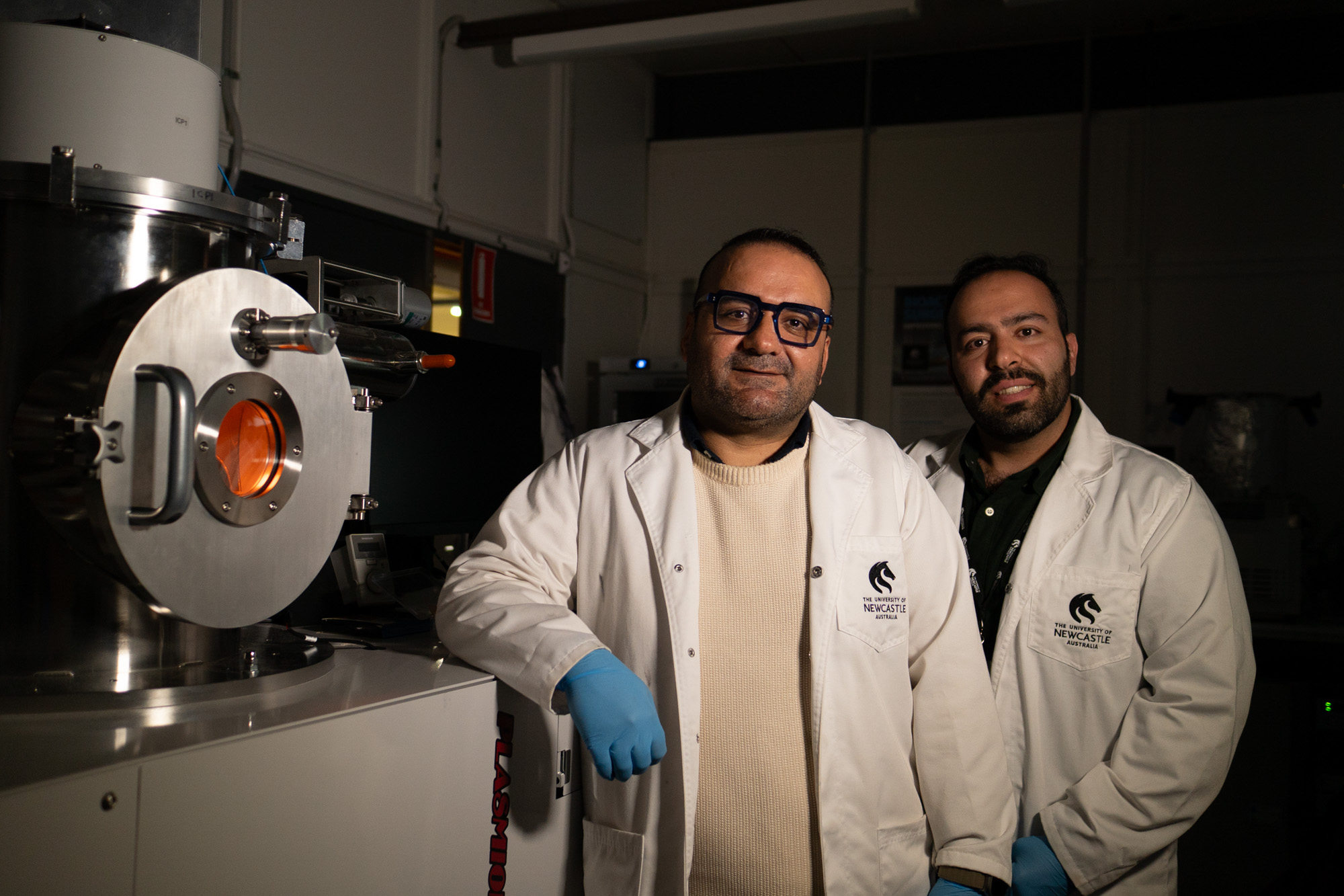 two researchers standing in a lab, wearing lab coats and smiling to camera