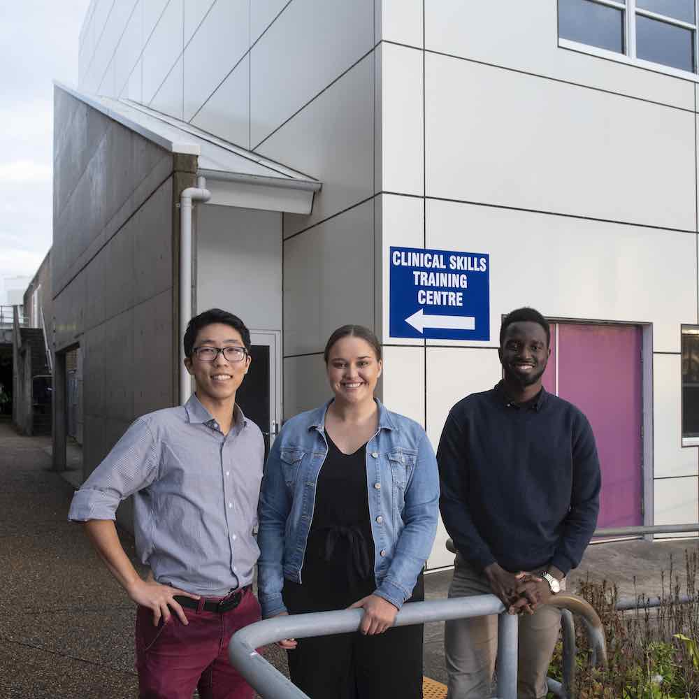 Three students standing at John Hunter Hospital, smiling at camera