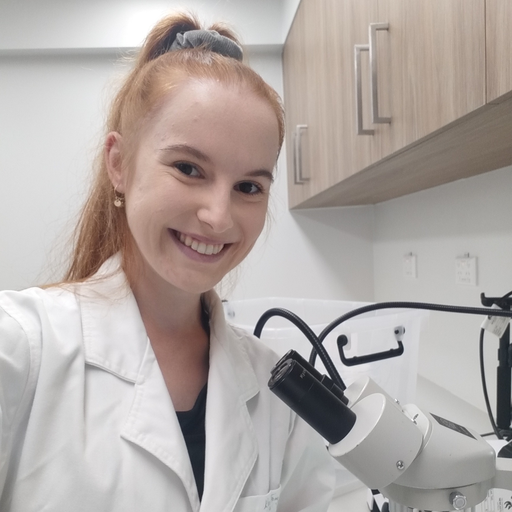 Alexandra Cottle smiling in a lab coat next to a microscope