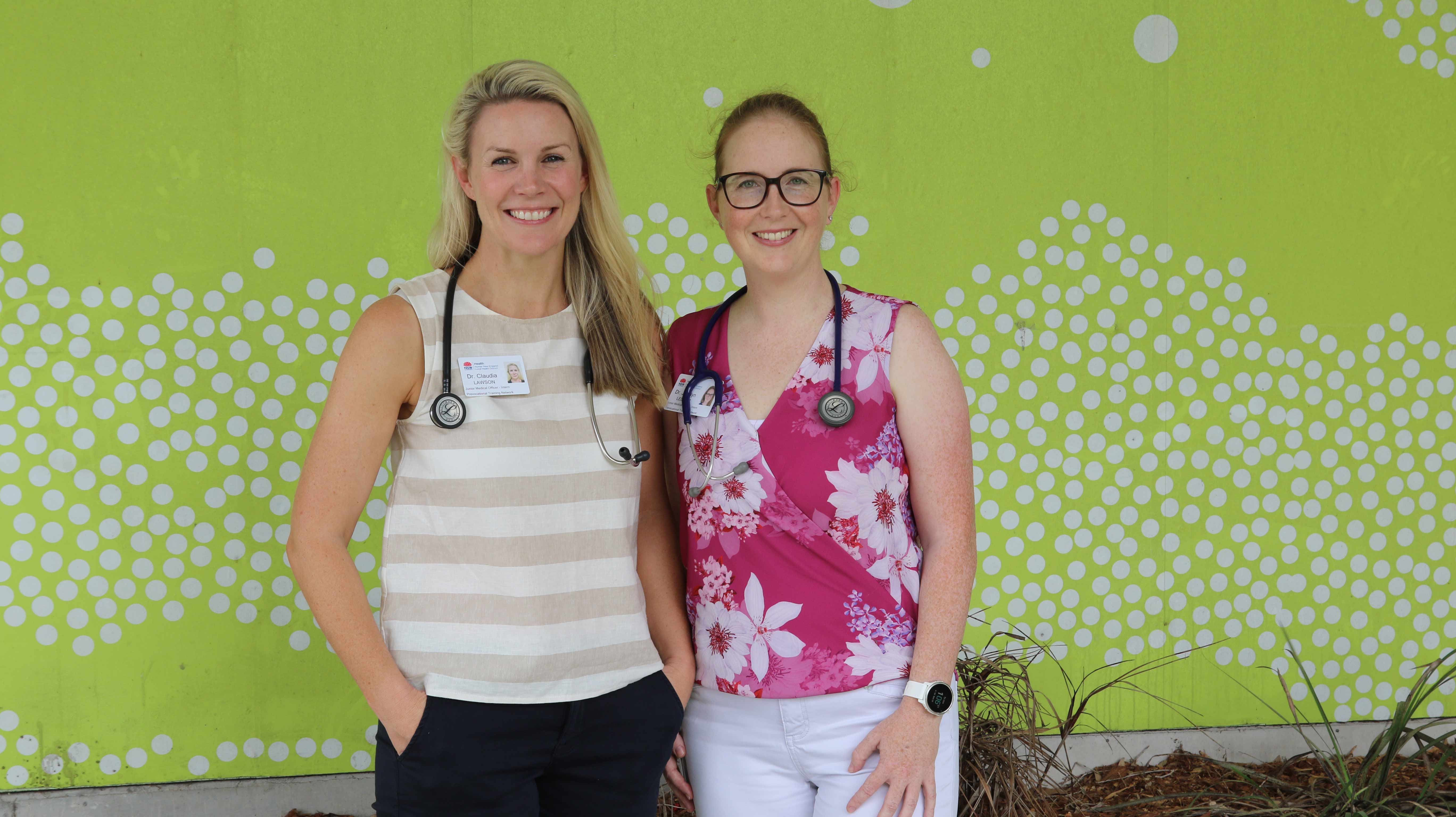 Two doctors stand with a green backdrop