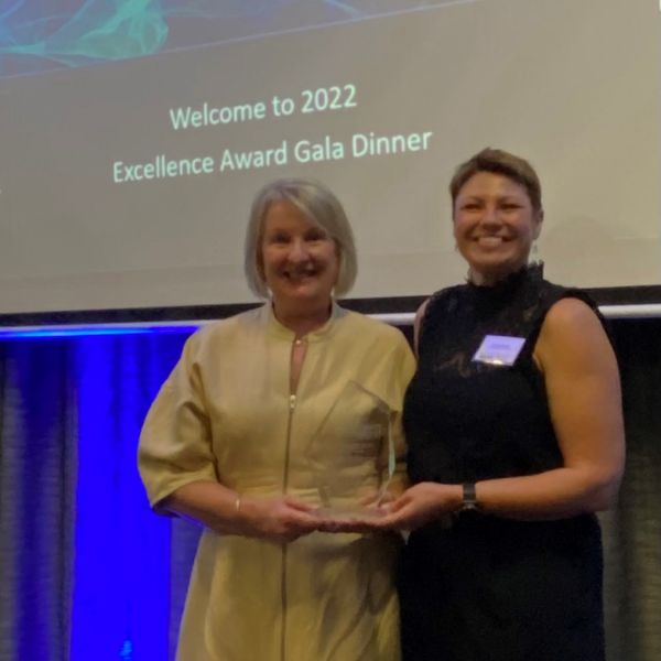Two women looking at the calendar at an awards ceremony holding a trophy. Quality Teaching Rounds recognised for Research Impact.