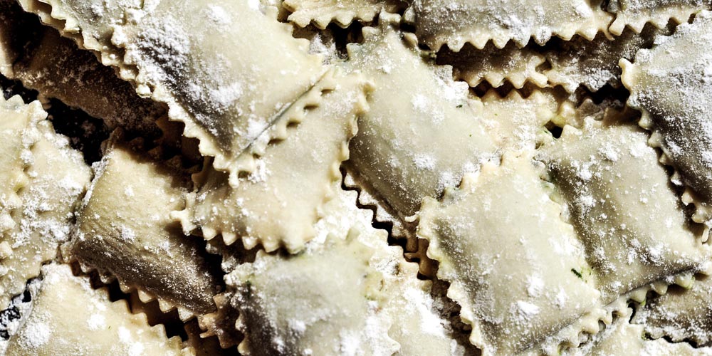 Approximately 20 pieces of uncooked ravioli pasta piled on top of each other.