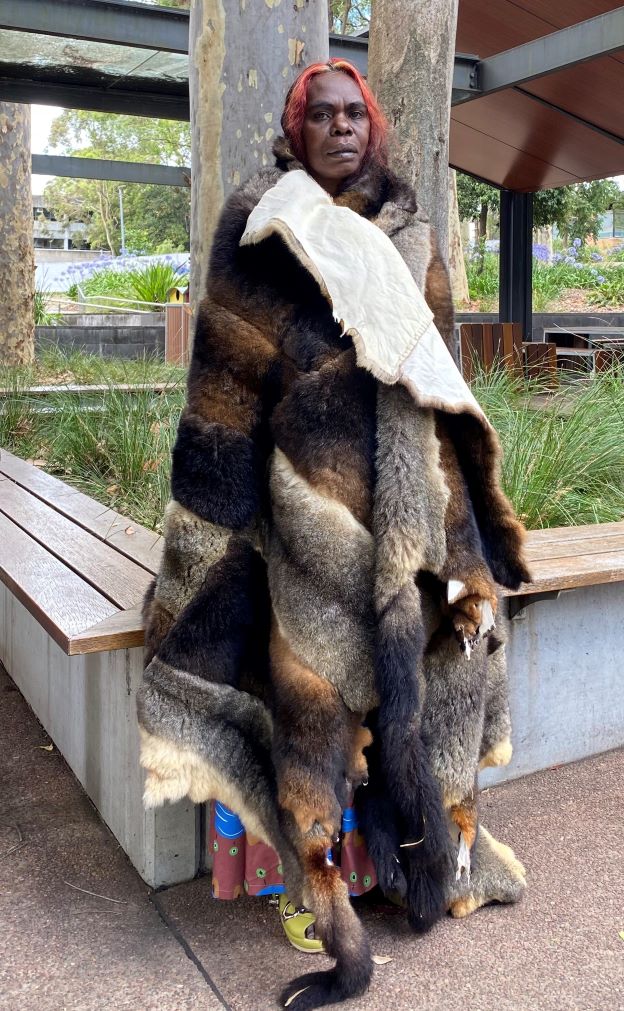 A full length shot of an Aboriginal woman wearing a possum skin cloak