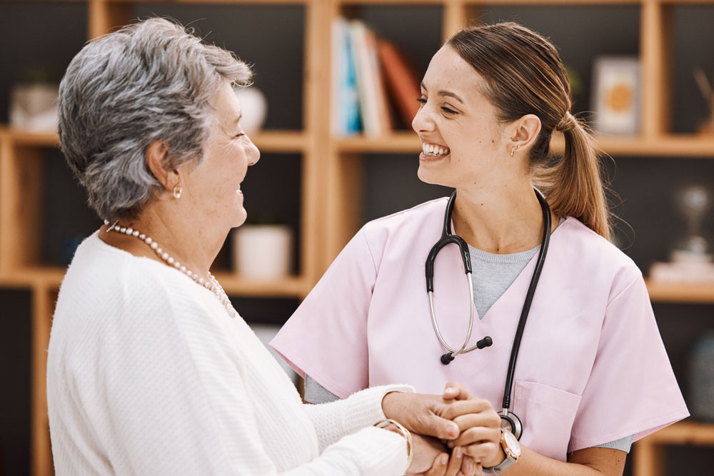 Nurse smiling at a patient with pink scrubs on and a blue stethoscope around her neck.