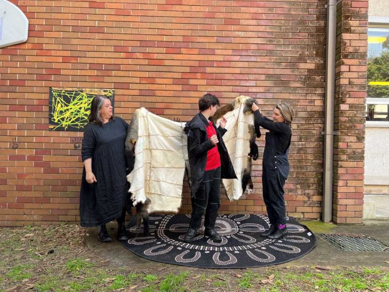 Students outside being wrapped in a completed possum skin cloak