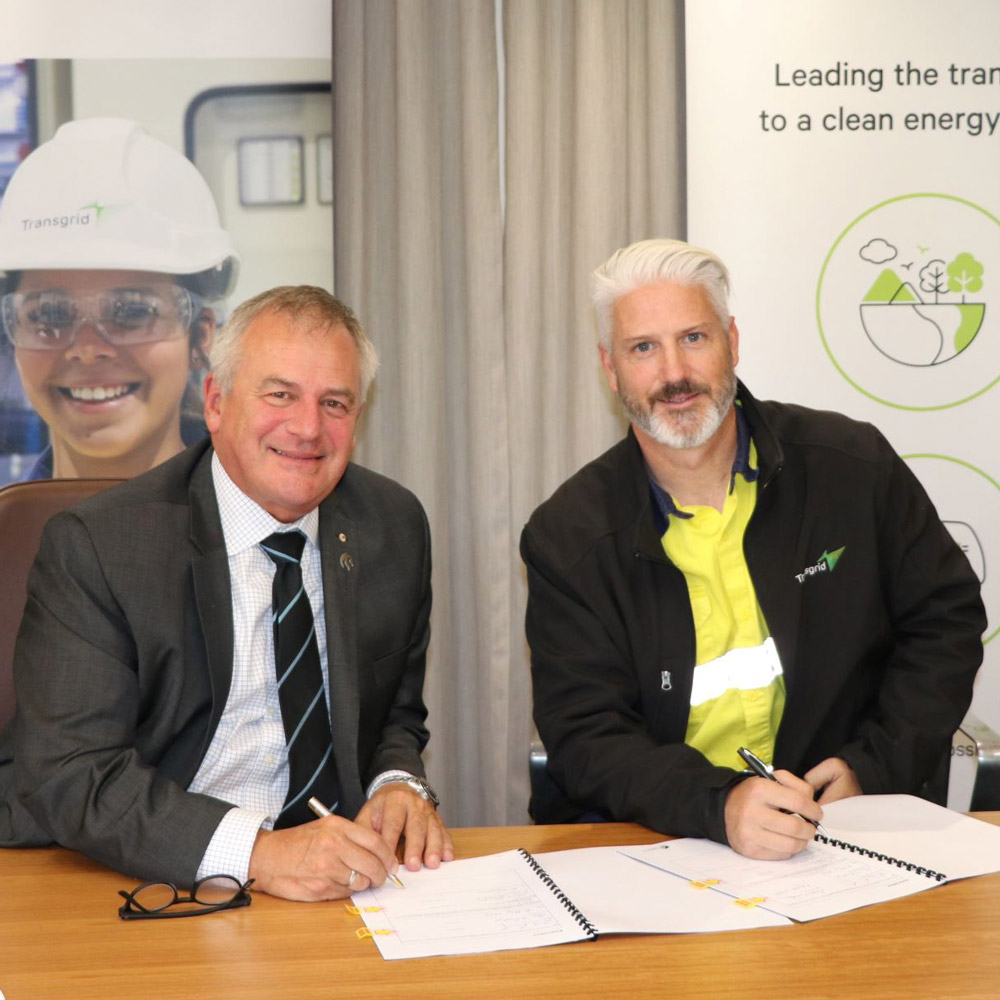 Vice Chancellor Alex Zelinsky and Transgrid's Craig Stallon sit at a desk with the MoU in front of them ready to sign the agreement