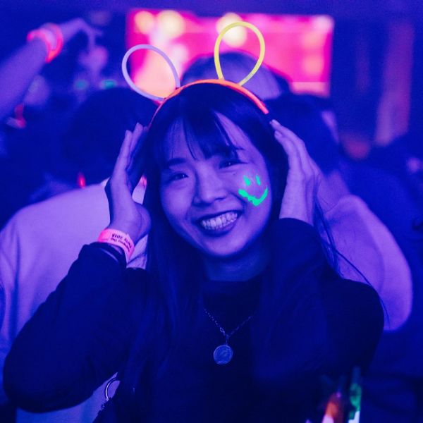 Student at the UNSA glow party with a smiley face facepaint and glow stick ears. 