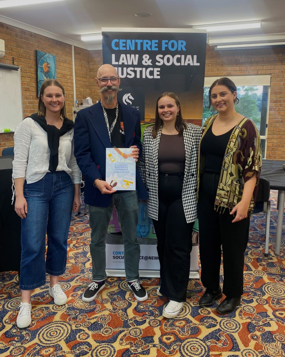 students with Associate Professor Kevin Sobel-Read pictured with the Indigenous Business Handbook in front of the Centre for Law and Social Justice banner