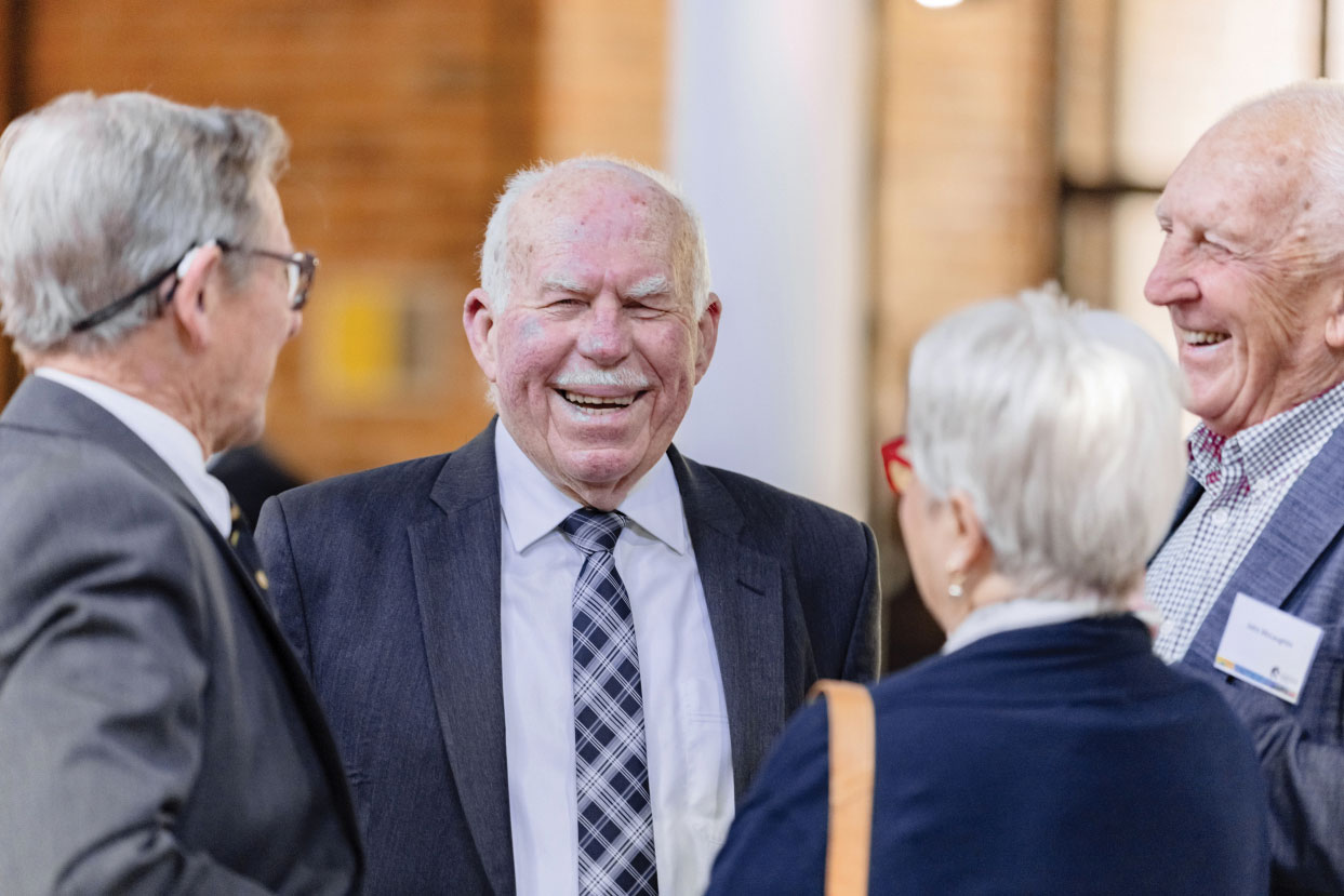 Chancellor Mr Paul Jeans speaking with donors at the 2023 Bequest Morning Tea. Smiling man in the camera's focus, talking to three other people standing around him