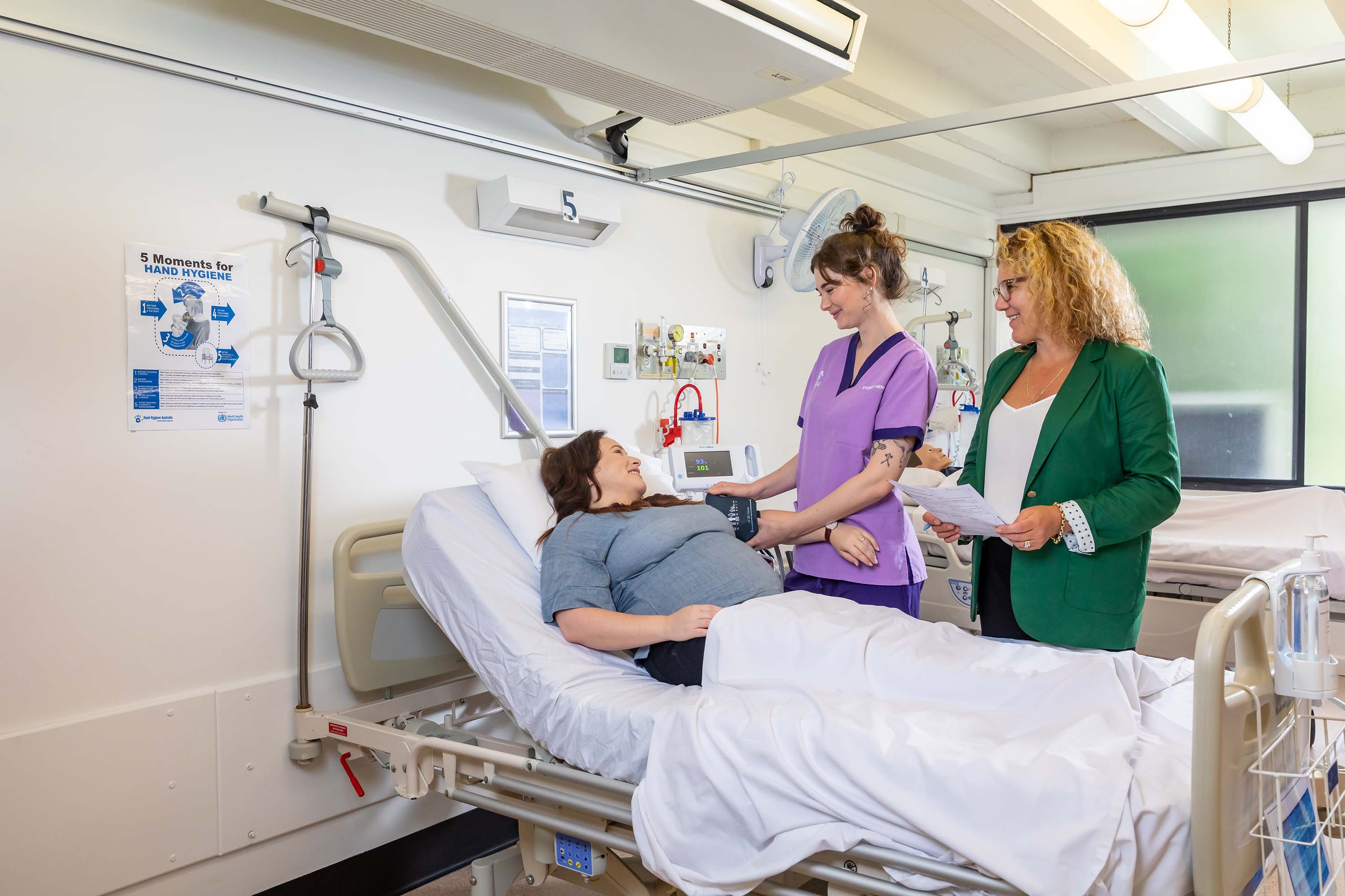 student, Nicole, pictured in a hospital setting assisting a patient in a bed