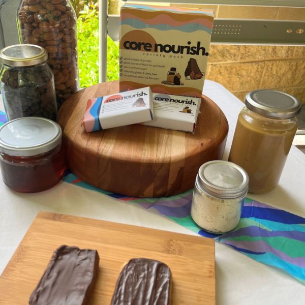 Two muesli bars sit on a chopping board on a table. On another chopping board is square packaging labelled 