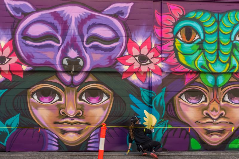 Woman spray painting a large colourful mural along a garage door