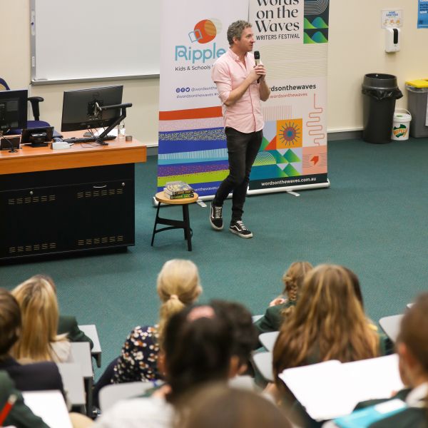 A man with a microphone addressing a room of students