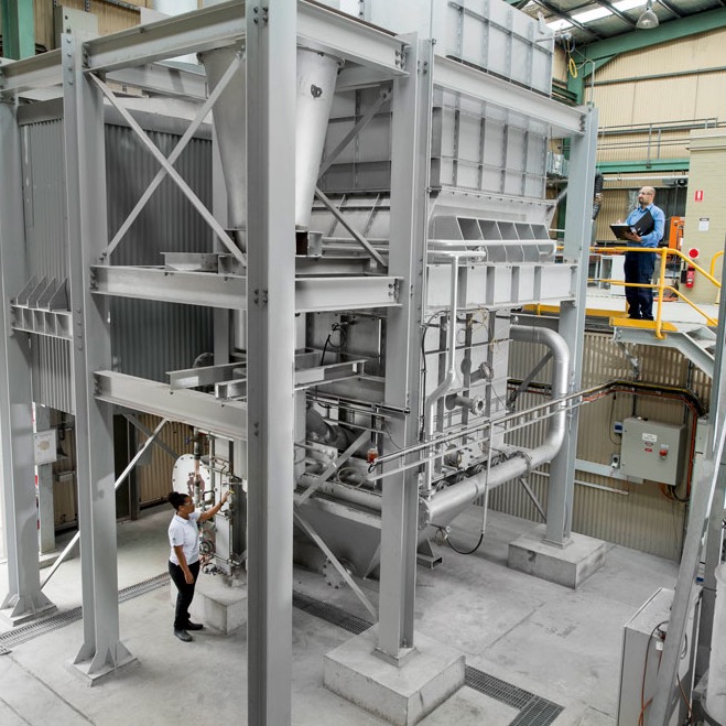 Two researchers standing at ground level and above ground level working on a large piece of chemical looping equipment